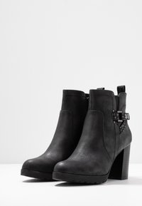 Botas negras hasta el tobillo hechas de cuero sintético texturizado, con un acento de hebilla geométrica y un tacón alto y robusto.
