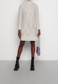 Abito a collo alto in maglia color crema con sfumature multicolori, lunghezza sopra il ginocchio. Abbinato a stivaletti neri alla caviglia e una piccola borsa lavanda.
