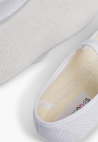 Weiße, Leinenschlüpfschuhe mit strukturiertem Obermaterial und einer glatten Gummisohle mit Blumenmustern. Das Innere zeigt ein Stofffutter mit Etikett.