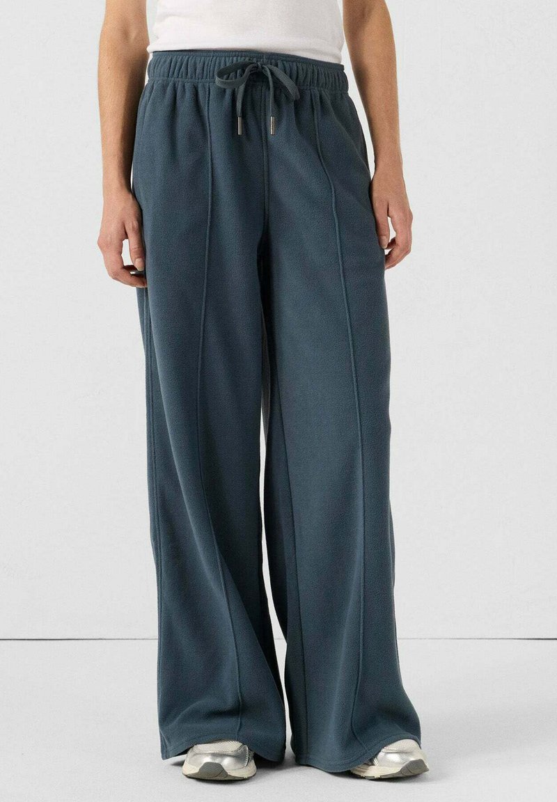 Donkergroen, wijde joggingbroek van zachte stof met een trekkoord in de taille. Heeft verticale stikdetails en een relaxte pasvorm.