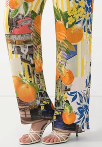 Pantaloni a gamba larga con un design colorato e fantasioso che include arance, fiori e forme geometriche. Il tessuto è morbido con una finitura lucida.