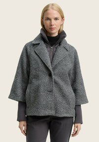 Grijze texturaal jasje met een boxy silhouet, puntige kraag, enkele knoopsluiting en ruime mouwen. De onderlaag heeft een hoge kraag.