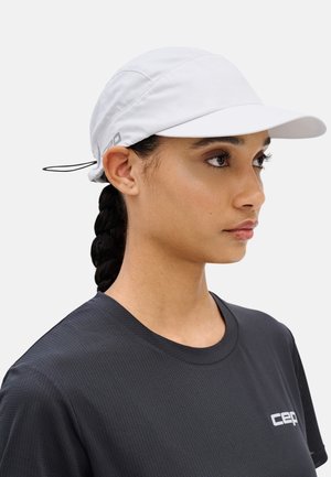Woman with braided hair wearing a white sport cap and a black crew-neck shirt with a small white logo on the chest.