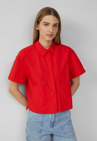 Czerwona koszula z krótkim rękawem, zapinana na guziki, z kołnierzykiem, z dwoma przednimi kieszeniami, wykonana z lekkiego materiału, zaprojektowana w skróconym fasonie.