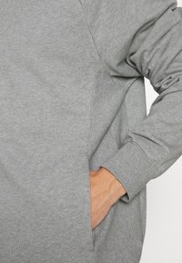 La felpa grigia chiaro presenta una texture morbida e una vestibilità comoda. Il design include una tasca laterale e polsini a coste.