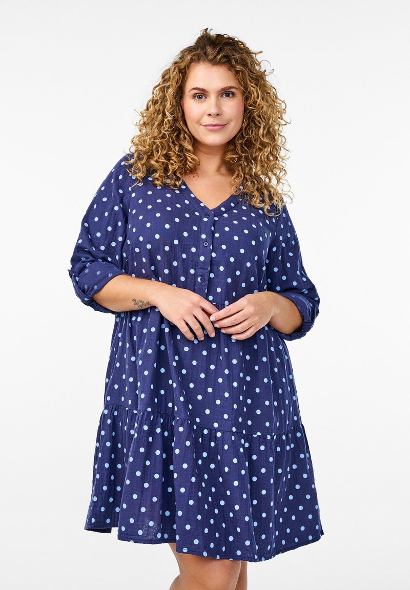 Marinekjole med lyseblå prikker, V-hals, knaplukning foran, lange ærmer og en lagdelt, vid flænsgant, lavet af et blødt, tekstureret stof.