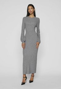 Lungo abito grigio a maglia con maniche lunghe, scollo a giro e silhouette aderente. Indossato con tacchi neri a caviglia.