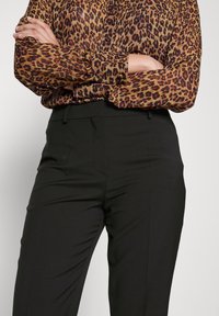 Blůza s leopardím vzorem v hnědé a černé barvě, s volným střihem. V kombinaci s dobře padnoucími černými kalhotami, vytvářející profesionální vzhled.