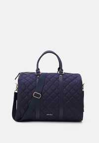 Mörkblå vadderad tygväska med dubbla handtag och justerbar axelrem, med guldaccent och en logotyp på framsidan.