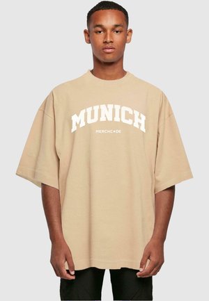 Béžové oversized tričko s nápisom "MUNICH" v tučných bielych písmenách naprieč hrudníkom. Vyrobené z mäkkej bavlny s krátkymi rukávmi.
