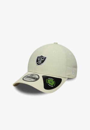 Gorra de béisbol beige con el logo de los Raiders bordado en la parte delantera. Presenta una visera curvada y una correa trasera ajustable. Textura suave.