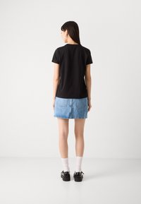 Top nero a maniche corte con scollatura tonda, abbinato a una gonna di jeans blu. Le calzature includono scarpe nere e calzini bianchi per un look casual.