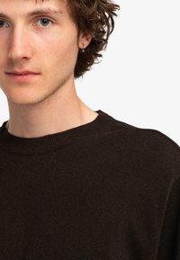 Dunkelbrauner Pullover mit einem gerippten Kragen und weicher Textur, der ein dezentes Stickdetail in der Taille aufweist.