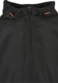 Veste noire avec fermeture éclair à l'avant et capuche ajustable avec cordons noirs et embouts orange.