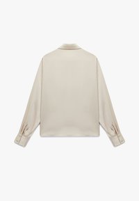 Camisa beige de manga larga hecha de tela suave. Presenta un collar estructurado y puños abotonados con un ajuste relajado y un diseño minimalista.