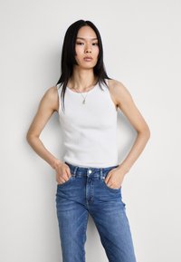 Λευκό ριβε ντεκολτέ τοπ με στρογγυλή λαιμόκοψη, συνδυασμένο με μπλε τζιν. Το ύφασμα είναι λείο με εφαρμοστό κόψιμο, αναδεικνύοντας ένα χαλαρό στυλ.