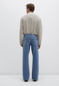 Striped long-sleeve shirt in beige and brown, paired with light blue wide-leg jeans featuring two back pockets and a brown leather patch.