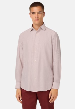 Camisa de botón de manga larga color rosa claro con un sutil patrón a rayas, cuello clásico y dobladillo redondeado, combinada con pantalones burdeos oscuros.