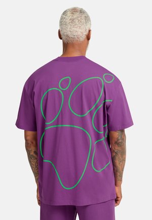 Lila kurzärmeliges T-Shirt mit einem großen grünen Pfotenabdruck auf der Rückseite. Hergestellt aus weicher Baumwolle, mit lockerem Schnitt und Rundhalsausschnitt.