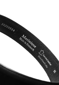 Fekete bőr öv sima felülettel. A "Matinique" márkanevének dombornyomott emblémáját és az anyag részleteit tartalmazza, beleértve a "Valódi bőr" és a "Nikkelmentes" feliratokat.