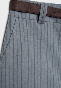 Gros plan sur un pantalon à rayures grises avec poche latérale inclinée et ceinture en daim marron foncé passant dans les passants.