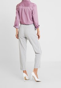 Light purple collared shirt, grey tapered pants with side stripes, and white high-heeled shoes, viewed from the back. Smooth fabric, casual fit.