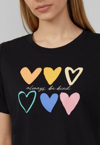 T-shirt en coton noir avec des formes de cœur colorées en orange, jaune, crème, sarcelle, bleu et rose, avec le texte "soyez toujours gentil" en dessous.