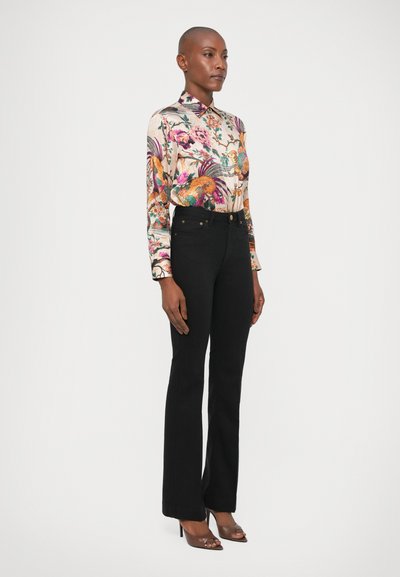 Camisa de manga larga con estampado floral en colores vibrantes, combinada con jeans negros de campana de cintura alta. Tacones con correa en el tobillo completan el conjunto.