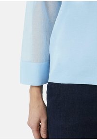 Hemelsblauw langemouwshirt met doorschijnende mesh mouwen en stevige manchetten, met een licht gestructureerde afwerking, gecombineerd met donkere denim.