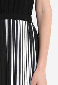 Schwarz-weißes Kleid mit vertikalen Streifen, elastischem Taillenbund und glatter Stoffoberfläche. Fokus auf das gemusterte Design und den Farbkontrast.