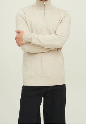 Ljusbeige polotröja med halv dragkedja, åtsittande ärmslut och en slät textur, kombinerat med svarta byxor.