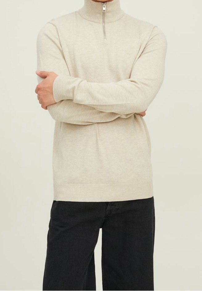 Ljusbeige polotröja med halv dragkedja, åtsittande ärmslut och en slät textur, kombinerat med svarta byxor.