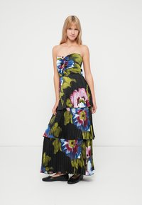Robe maxi noire plissée sans bretelles avec un motif floral vibrant en vert, rose et bleu. Présente des volants en couches et un corsage ajusté.