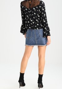 Blusa nera floreale con schiena in pizzo, abbinata a una gonna di jeans aderente con orlo sfilacciato. Il modello indossa stivaletti neri.