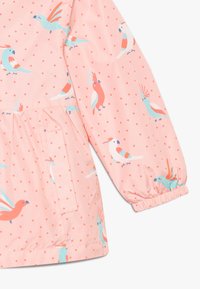 Růžová rukávová část bundy a kapsa s elastickým manžetovým zakončením, potištěná barevnými kreslenými papoušky a malými červenými puntíky.