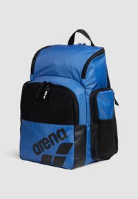 Mochila de nailon azul con un bolsillo frontal de malla, acentos negros, detalle del logotipo y múltiples compartimentos con cremallera. Correas acolchadas para mayor soporte.