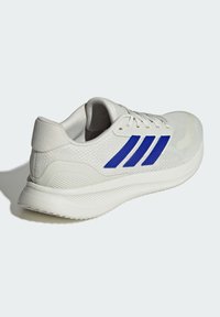 Zapatilla deportiva blanca con diseño de tres rayas azules, parte superior de malla, talón texturizado y suela acolchada para mayor comodidad y soporte.