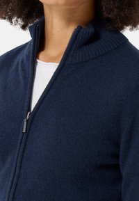 Marineblauer Reißverschluss-Pullover mit geripptem Kragen und weichem Textil. Mit einem silbernen Reißverschluss und einem lässigen, entspannten Schnitt. Ideal zum Layering.