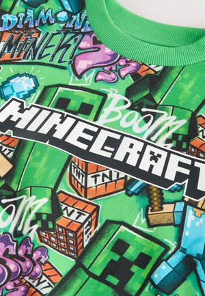 Zelené bavlnené tričko s dizajnom Minecraftu s pixelovými postavami, textom „Boom“ a „Minecraft“ v tučnom čiernom písme na farebnom pozadí.