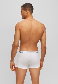 Caleçons blancs en coton avec un logo "BOSS" noir sur la ceinture, présentant un design ajusté et un tissu lisse. Le modèle est vu de dos.