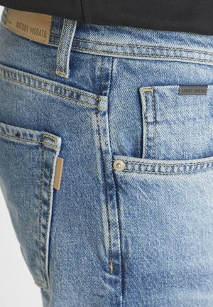 Light blue denim jeans with a faded finish, five pockets, visible stitching, and a leather label on the waistband. Features a snap closure.
