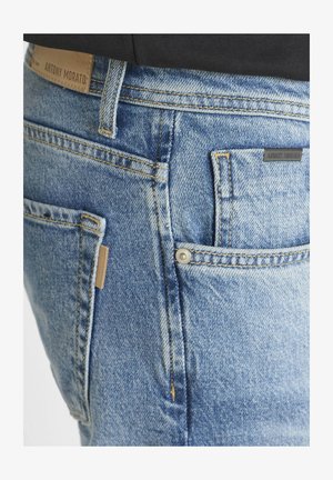 Light blue denim jeans with a faded finish, five pockets, visible stitching, and a leather label on the waistband. Features a snap closure.