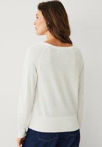 Maglione bianco a maglia con scollatura ampia, orlo a coste e dettagli di cucitura laterale, abbinato a jeans blu scuro. Texture liscia, vestibilità casual.