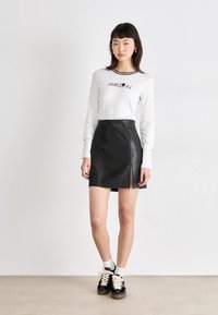 Mini falda de cuero negro con una abertura frontal, combinada con una blusa blanca de manga larga que tiene un cuello a rayas negras. Incluye calzado casual.