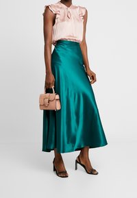 Turkos satinmaxikjol kombinerad med en rosa ruffled blus och en liten handväska i blushfärg. Öppen tå svarta klackar fulländar looken.