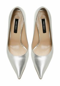 Zilveren hoge hakken met een spitse neus, een gladde metallic textuur, open zijkanten en een merkje op de binnenzool.