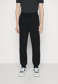 Pantalones de chándal negros con cintura elástica y cordón, con tobillos ajustados. Combinados con zapatillas negras, blancas y azules.