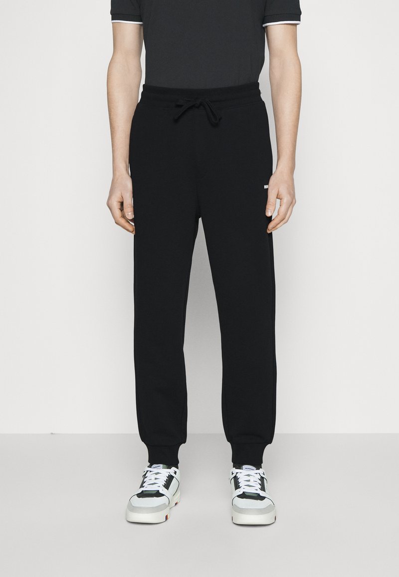 Pantalones de chándal negros con cintura elástica y cordón, con tobillos ajustados. Combinados con zapatillas negras, blancas y azules.