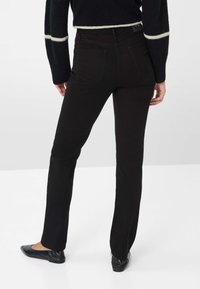 Jeans neri a gamba dritta con tasche posteriori, vita media e una consistenza liscia. Abbinati a scarpe nere senza tacco.