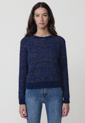 Suéter de punto azul marino con un patrón texturizado, cuello redondo y puños acanalados. Combinado con jeans de color azul claro.